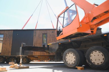 Crane operatörü, modern inşaat ve ulaşım yöntemlerini gösteren prefabrik modüler evi kamyona yüklüyor.