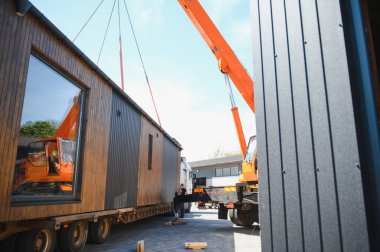 Vinç prefabrik modüler evi kamyona yüklüyor, verimli ve modern bina ulaşımını sağlıyor.