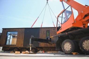 Crane operatörü prefabrik modüler evi kamyona yüklüyor, modern inşaat ve taşımacılıkta verimlilik ve yenilik sergiliyor