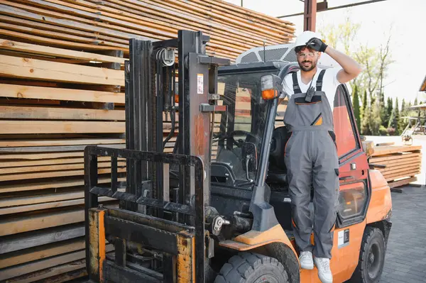Kereste deposunda kendine güvenen bir depo çalışanı, kereste yığınlarıyla çevrili, ahşap işlemede profesyonelliği ve uzmanlığı gösteriyor.