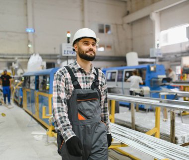 Üniforma giyen sanayi işçisi modern pencere ve kapı fabrikasında üretim hattı boyunca yürüyor.