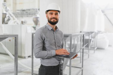 Kask takan mühendis, gıda işleme tesisinde üretim yaparken dizüstü bilgisayar kullanıyor.