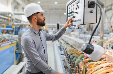 Modern bir fabrikada sabit kasklı çalışma makineleri takan endüstri mühendisi sorunsuz bir üretim süreci ve kalite kontrolü sağlıyor.