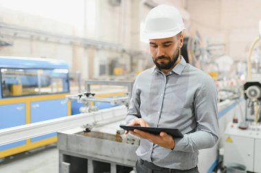 Modern pvc ve alüminyum pencere ve kapı fabrikalarında otomatikleştirilmiş üretim hattını kontrol ederken dijital tablet kullanan sabit kasklı üretim denetleyicisi