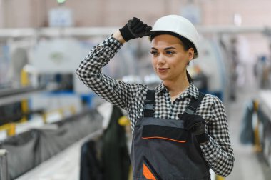 Endüstriyel imalat fabrikasında üretim bandı üzerinde çalışırken koruyucu başlığını düzelten kendine güvenen kadın fabrika işçisi.