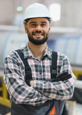 Kollarını kavuşturup gülümseyen kendinden emin endüstriyel işçiler, yoğun bir fabrika ortamında profesyonellik ve uzmanlık gösteriyorlar.