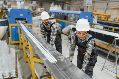 İki fabrika işçisi modern bir üretim bandında üretilen PVC pencere ve kapı çerçevelerinin kalitesini kontrol ediyor.