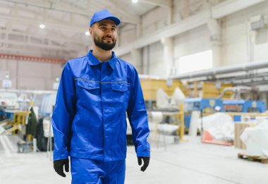 Kendine güvenen fabrika işçisi modern üretim hattında üniforma ve şapkayla yürüyor PVC ve alüminyum pencere ve kapılar üretiyor.