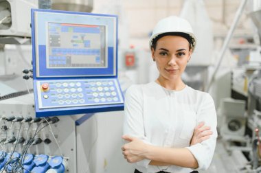 Çapraz kolları olan ve modern bir fabrikada üretim hattını denetleyen kendinden emin kadın mühendis.