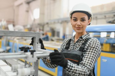 Güvenlik kaskı ve eldiven takan kadın işçi pencere ve kapı imalat fabrikasında endüstriyel makineler çalıştırıyor.