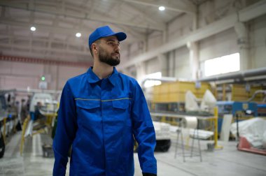 Modern bir PVC ve alüminyum pencere fabrikasında mavi üniformalı ve şapkalı bir yönetici üretim hattını kontrol ediyor.