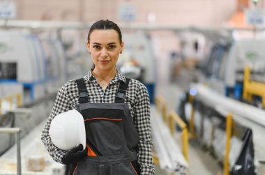 Kendine güvenen kadın fabrika işçisi kaskını tutuyor, modern bir PVC pencere ve kapı üretim tesisinde duruyor.