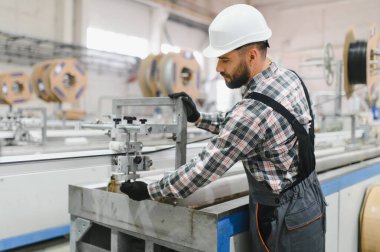 Güvenlik kaskı ve eldiven takan fabrika işçisi. PVC pencere ve kapı üretim hattında çalışan makineler.