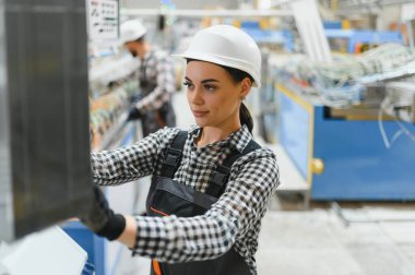 Kendine güvenen kadın mühendis tulum giyiyor ve modern fabrika ortamında endüstriyel makineler çalıştırıyor.