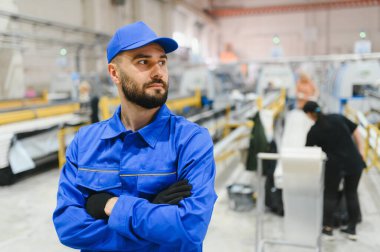 Bir pencere ve kapı fabrikasında çapraz silahlarla duran kendinden emin bir yöneticinin portresi, üretim sürecini denetliyor.