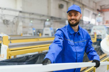 Gülümseyen fabrika işçisi, pencere ve kapı üretim tesisinde yeni üretilmiş bir PVC pencere çerçevesi taşıyor.