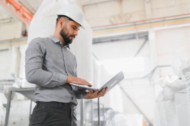 Endüstriyel mühendis, bir gıda işleme tesisinde operasyonları denetlerken dizüstü bilgisayar kullanıyor.