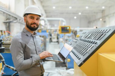 Modern fabrikadaki üretim hattını denetlerken kontrol panelinin yanına dizüstü bilgisayar kullanan sanayi mühendisi.