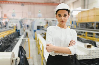Pencere ve kapı fabrikasında çapraz kollu, kendinden emin kadın mühendis. Üretim sürecini denetliyor.