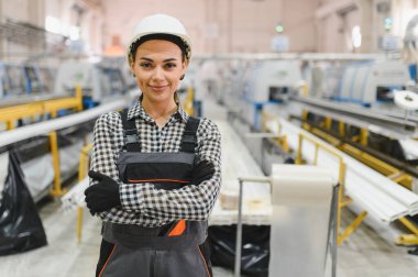 Güvenli kask ve tulum giyen, modern bir fabrikada kolları çapraz duran kendine güvenen kadın endüstriyel işçiler.