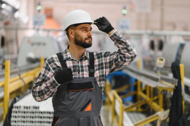 Bir imalat fabrikasında çalışırken kaskını düzelten sanayi mühendisi, güvenlik ve üretim süreçlerini denetliyor.