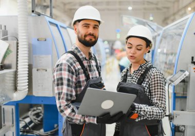 Diz üstü bilgisayar kullanan ve plastik pencere ve kapı fabrikasında iş tartışan iki mühendis.