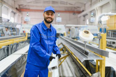 Gülümseyen fabrika işçisi pencere ve kapı imalatı için üretim hattında alüminyum profillere bakıyor.