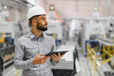 Dijital tablet kullanan, modern fabrikada işletim ve üretim sürecini yöneten sanayi mühendisi.