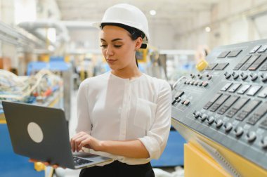 Modern fabrikada üretim hattını yönetmek için dizüstü bilgisayar kullanan kadın endüstriyel mühendis.
