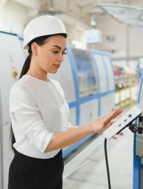 Modern endüstriyel fabrika üretim hattında kadın mühendis sabit kasklı kontrol paneli takıyor.