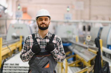 PVC ve alüminyum pencere ve kapı üretim hattında duran baret ve tulum giyen bir fabrika işçisinin portresi