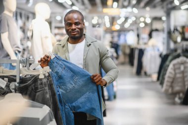 Bir giyim mağazasında alışveriş yaparken kotları karıştıran müşteri, modern bir perakende piyasasında gündelik ve modaya uygun bir deneyimin tadını çıkarıyor.