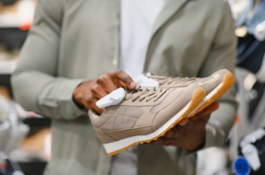 Moda mağazasında alışveriş yaparken moda bej ayakkabıları inceleyen şık bir adam, mükemmel ayakkabıları seçme tecrübesinin tadını çıkarıyor.