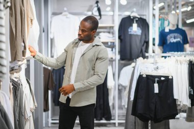 Giysi mağazasında gömlek seçen şık bir adam, alışveriş deneyiminin ve modern perakende satış ortamının tadını çıkarıyor.