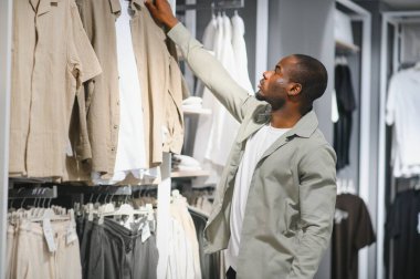 Müşteri perakende mağazasında elbise raflarını karıştırıyor. Gardırobunu ve tarzını geliştirmek için en uygun gömleği arıyor.