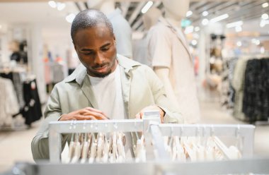 Modern moda mağazasında elbise seçen şık bir Afro-Amerikan erkeği alışveriş merkezindeki alışveriş deneyiminin tadını çıkarıyor.
