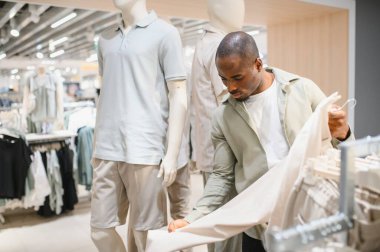 Modern moda mağazasında kıyafet seçen şık bir Afro-Amerikan erkeği alışveriş merkezinde alışveriş deneyiminin tadını çıkarıyor.