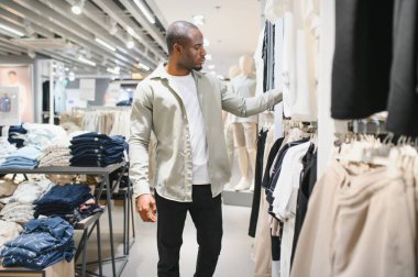 Modern moda mağazasında kıyafet seçen şık bir Afro-Amerikan erkeği alışveriş merkezinde alışveriş deneyiminin tadını çıkarıyor.