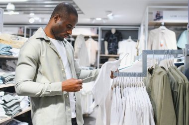 Afro-Amerikalı bir adam alışveriş merkezinde kıyafet seçeneklerini araştırıyor. Moda ve tarz seçimlerine odaklanıyor.