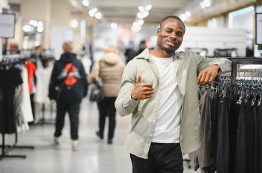 Afrika kökenli Amerikalı bir adam alışveriş merkezinde kıyafet seçeneklerini araştırıyor. Moda anlayışını ve tarzını alışverişte sergiliyor.