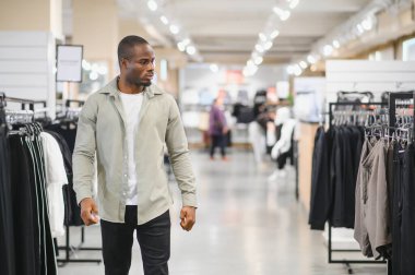 Bir giyim mağazasında gezen şık bir adam, en son modern giyim koleksiyonuna göz atıyor ve hareketli alışveriş atmosferinin tadını çıkarıyor.