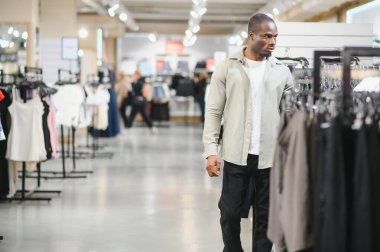 Müşteri büyük bir giyim mağazasına göz atıyor, şık kıyafetler seçiyor ve hareketli bir alışveriş ortamında çeşitli seçenekleri keşfediyor.