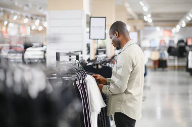 Müşteri elbise raflarını karıştırıyor, canlı bir perakende mağazasında şık kıyafetler seçiyor, çeşitli moda tercihlerinin keyfini çıkarıyor.