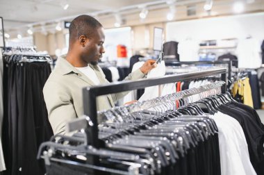 Müşteri, modern bir alışveriş merkezindeki giyim mağazalarına göz atıyor. Çeşitli seçenekler arasından şık bir beyaz gömlek seçiyor.