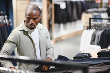 Bir giyim mağazasında gezinen şık bir adam, canlı bir alışveriş merkezinde son moda trendlerini alırken yeni pantolon seçiyor.