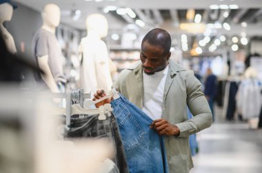 Perakende mağazasından kot pantolon seçmeye odaklanmış müşteriler, çeşitli kıyafetlerle donatılmışlar.