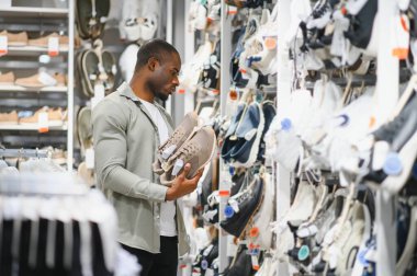 Bej ayakkabılar tutan şık bir adam, perakende mağazasında ayakkabı alışverişi yapan, satın alma kararları veren.