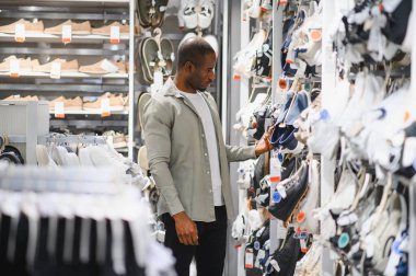 Bir perakende mağazasında ayakkabıları karıştıran şık bir adam koleksiyonu için çeşitli moda tarzları ve markaları göz önünde bulundurur.