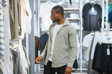 Modern moda mağazasında kıyafet seçen şık bir Afro-Amerikan erkeği alışveriş merkezinde alışveriş deneyiminin tadını çıkarıyor.