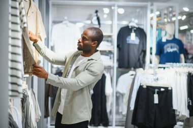Müşteri perakende mağazasında alışveriş yaparken giysi seçeneklerini inceliyor. Modern bir gardırop için şık kıyafetler seçiyor.